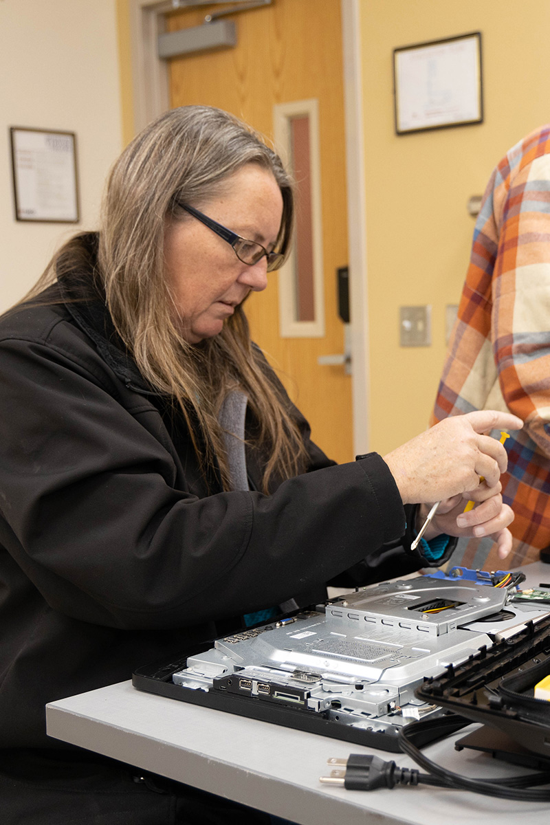 A women, screwdriver in hand, works on dismantling a computer mainframe.