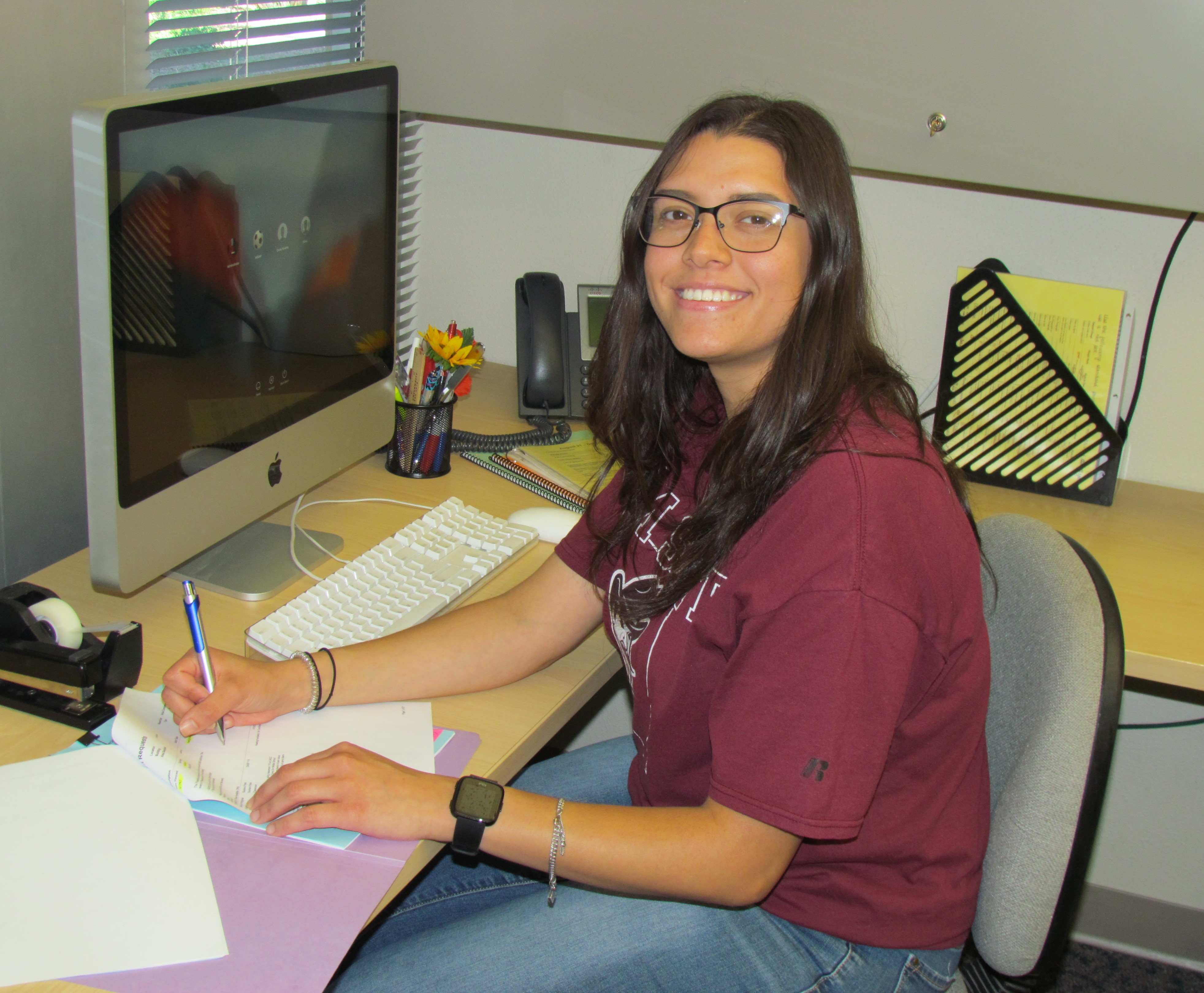 An NMSU Aggie breaks from filling out a document on her desk to give a smile.