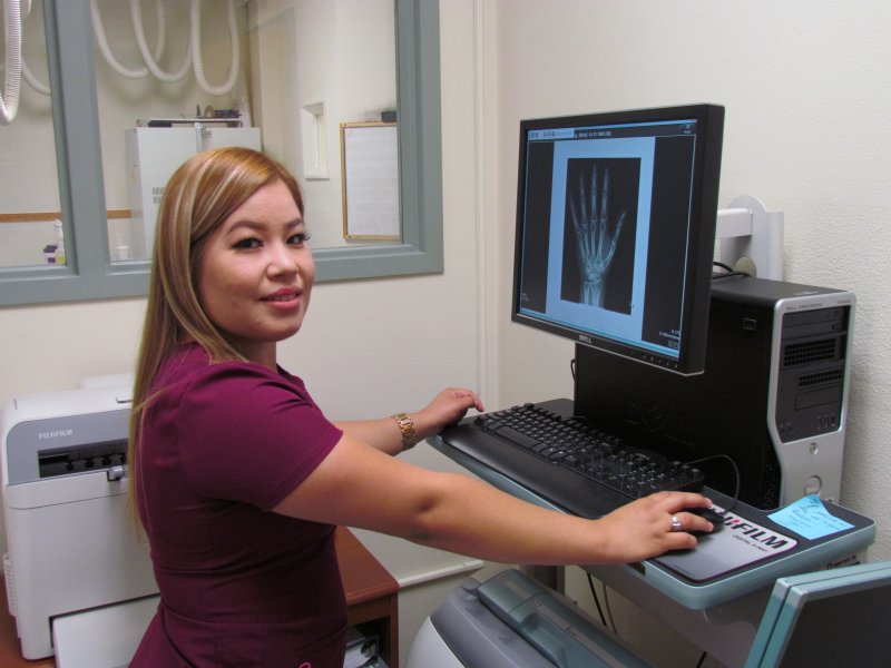 A radiologic technologist smiling back at the viewer from a hand x-ray she has produced on a computer monitor